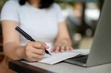 Hafta sonları bir kafede çalışan, not defterine not alan, işini yöneten ve bilgisayarını kullanan bir kadının görüntüsü..