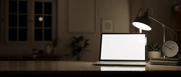 Workspace at night, a laptop white screen mockup to display your graphic on screen, a table lamp, and decor on a desk. 3d render, 3d illustration