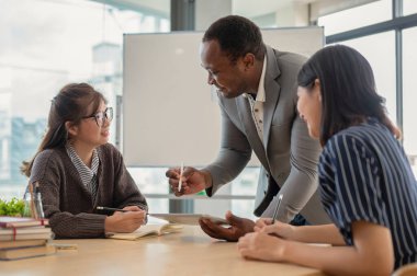 Profesyonel bir Afrikalı Amerikalı işadamı ya da erkek patron Asyalı çalışanları toplantı odasında eğiterek beyin fırtınası ve brifing projesi yapıyor. Çeşitli iş arkadaşları.