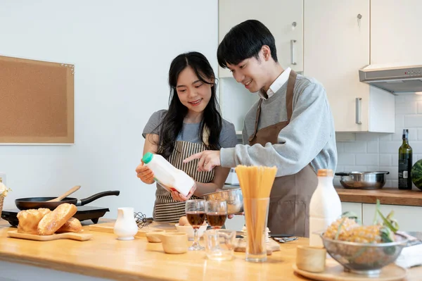 Happy and lovely young Asian couple making pancakes, mixing pancake flour in a lovely minimal kitchen together. enjoy cooking, spending time together, lifestyle concept