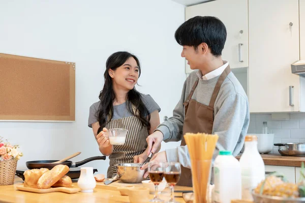 A lovely and joyful young Asian couple enjoys baking pastry or making pancakes in the kitchen together. cooking dates at home, leisure, family activity