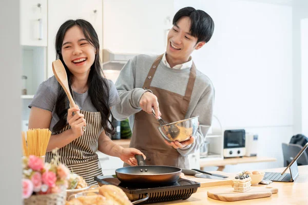 A lovely and joyful young Asian couple is laughing, playing, enjoying baking pastry, or making pancakes in the kitchen together. cooking dates at home, leisure, family activity