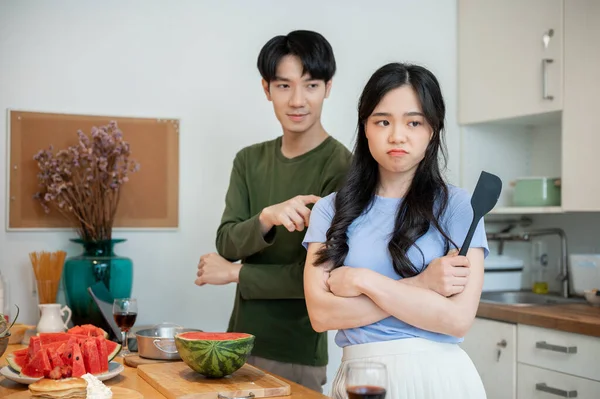 A cute, clingy young Asian boyfriend is asking for forgiveness from his angry girlfriend after arguing while cooking in the kitchen together. Lover, married, domestic life