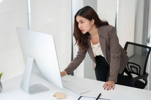 プロフェッショナルで焦点を当てたアジアのビジネスマンがテーブルの上に曲がり 彼女のコンピュータ画面を見て 彼女のプライベートオフィスで彼女の机で働いています — ストック写真