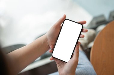 Bulanık bir arkaplan üzerinde akıllı telefon beyaz ekran maketi tutan bir kadının üst görüntüsü. Bir kadın kahve dükkanındaki masada otururken akıllı telefonunu kullanıyor..