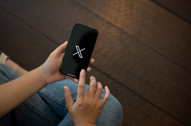 Tayland, Chiang Mai - 23 Ağustos 2023: Bir kafedeki masada otururken Twitter X uygulaması kullanan bir kadın.