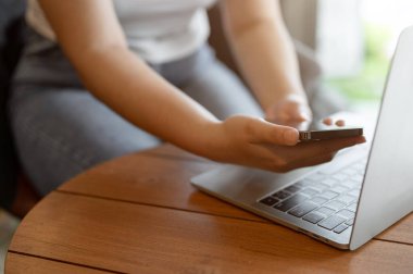 Bir kafede uzaktan çalışan, akıllı telefonunu ve laptopunu masada kullanan bir kadın serbest çalışanın yakın plan görüntüsü..