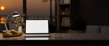 Çalışma odası, beyaz dizüstü bilgisayar, masa lambası ve penceresinde güzel bir günbatımı manzarası olan karanlık, modern bir oturma odasında aksesuarlar. 3d görüntüleme, 3d illüstrasyon