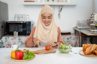 Güzel bir Asyalı Müslüman kadın salata karışımı için mutfakta malzeme hazırlıyor, domates doğruyor, mutfakta yemek pişiriyor..