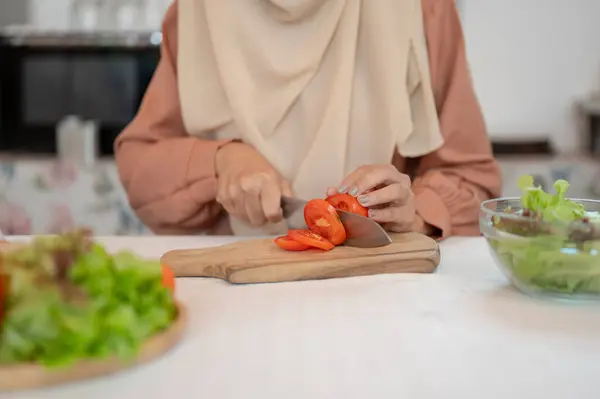 ムスリム女性のクローズアップ画像は キッチンでサラダミックス用の食材を準備し チョッピングボードにトマトをカットし キッチンで料理しています レジャー ライフスタイル — ストック写真