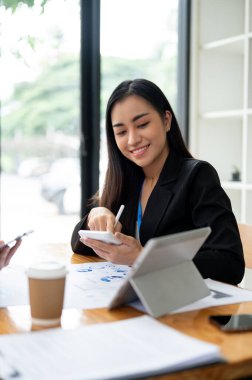 Harika bir Asyalı iş kadını ya da kadın muhasebeci hesap makinesi kullanıyor, finansal verileri analiz ediyor ve iş arkadaşıyla ofiste çalışıyor..