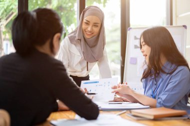 Çekici ve kendinden emin Asyalı Müslüman bir iş kadını ya da tesettürlü kadın bir yönetici takımının fikirlerini dinliyor ve toplantıda onlarla birlikte yeni bir proje üzerinde fikir alışverişinde bulunuyor. Çeşitli iş adamları