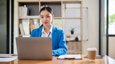 Kendine güvenen ve profesyonel Asyalı bir iş kadını ya da mavi takım elbiseli bir kadın finans asistanı dizüstü bilgisayarının klavyesinde yazı yazıyor, ofisinde bilgisayarında çalışıyor..