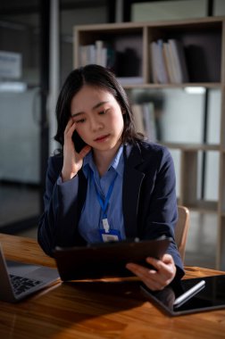 Resmi takım elbiseli düşünceli ve odaklanmış Asyalı bir iş kadını ya da bayan yönetici ofisinde masasında evrakları okuyor..