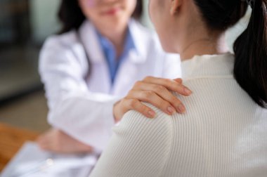 İlgili bir kadın doktor ya da psikiyatristin yakın plan görüntüsü bir hastanede semptomlar ve tedavi planları hakkında konuşurken hastanın omzuna dokunur..