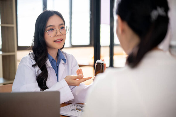A beautiful and professional Asian female doctor is showing and describing pills to a female patient during an appointment at a hospital. medicine prescription, offer new medicines