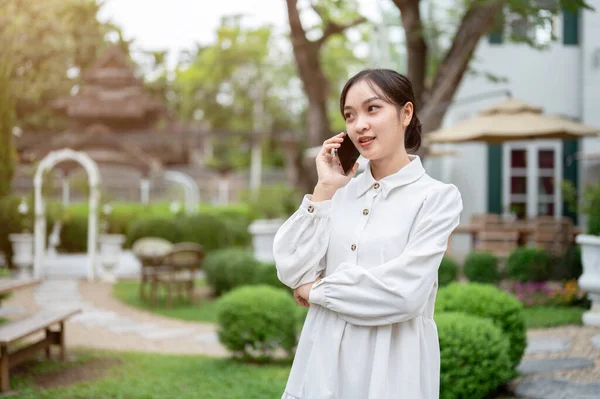 아름다운 아시아 여성은 아름다운 정원이나 뒤뜰에서 휴식을 취하면서 누군가와 전화로 — 스톡 사진