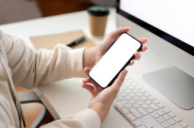 Ofisindeki masasında otururken akıllı telefonunu kullanan serbest çalışan bir kadının yakın plan görüntüsü. akıllı telefon beyaz ekran modeli