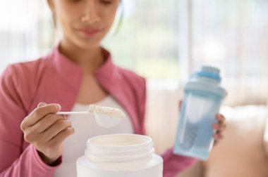 Close-up image of a healthy and fit Asian woman in sportswear making her protein shake after a workout at home. Drink supplements, high-nutrition drinks, diet, and muscle-building clipart