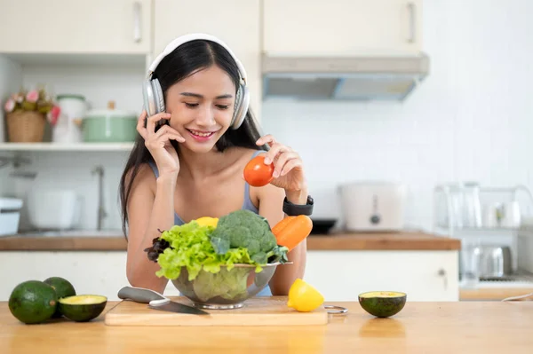 ジムの服で幸せで美しいアジアの女性は キッチンで彼女の健康的な朝食とスムージーを準備しながらヘッドフォンで音楽を楽しんでいます — ストック写真