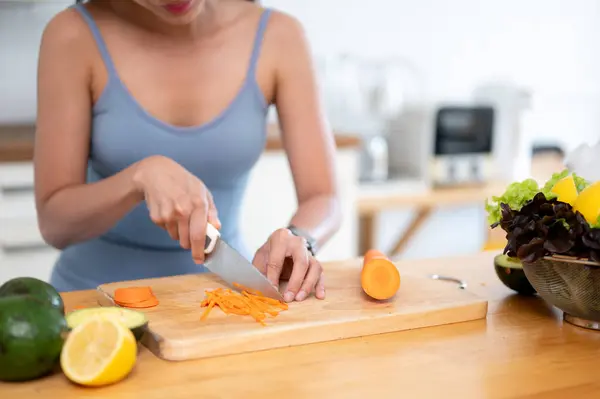 ジム服の健康でフィット感のある女性のクローズアップ画像は チョッピングボードにニンジンをスライスし キッチンでジムの後に彼女の健康的な朝食のための食材を準備しています 健康的なライフスタイルのコンセプト — ストック写真