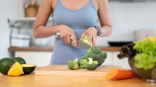 ジム服の健康でフィット感のある女性のクローズアップ画像は チョッピングボードにブロッコリーを切って キッチンで彼女の健康的な朝食のための食材を準備しています クッキングと健康的なライフスタイル — ストック写真