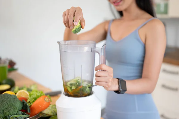 Close-up image of a beautiful and fit young Asian woman in gym clothes making her healthy green smoothie in the kitchen after her workout. Healthy lifestyle, wellbeing, urban life, That girl trend