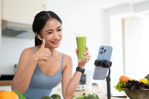 魅力的なアジアの女性インフルエンサーまたはオンライン栄養コーチは 彼女のオンラインフォロワーと彼女の健康的な緑のスムージーレシピを共有しています — ストック写真