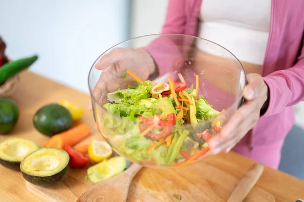 キッチンテーブルの上に健康的な新鮮なサラダのボウルを保持するスポーツウェアの女性のクローズアップ画像 健康的な食べ物 食事療法 調理する — ストック写真