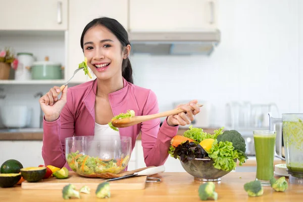 スポーツウェアの魅力的で陽気なアジアの女性は キッチンのキッチンテーブルで彼女の健康的なサラダを楽しんでいます 健康的なライフスタイルのコンセプト — ストック写真