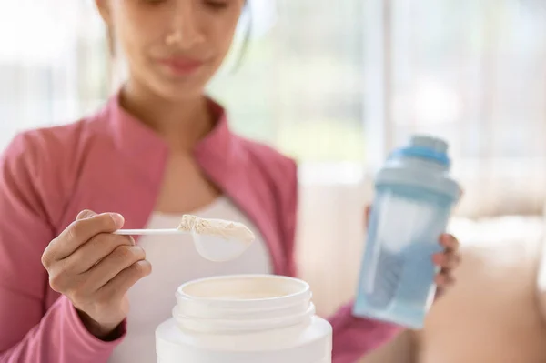 Spor kıyafetli sağlıklı ve formda bir Asyalı kadının evde yaptığı egzersizden sonra protein içeceğini yakından çekerken görüntüsü. İçki takviyeleri, yüksek besleyici içecekler, diyet ve kas geliştirme.