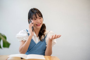 Hoş ve neşeli bir Asyalı kadın bir kafede dinlenirken arkadaşlarıyla telefonda konuşuyor..