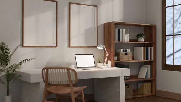 A minimalist white home office workplace with a laptop mockup on a white table against the white wall with blank frames mockup, a wooden chair, and a wooden bookshelf. 3d render, 3d illustration