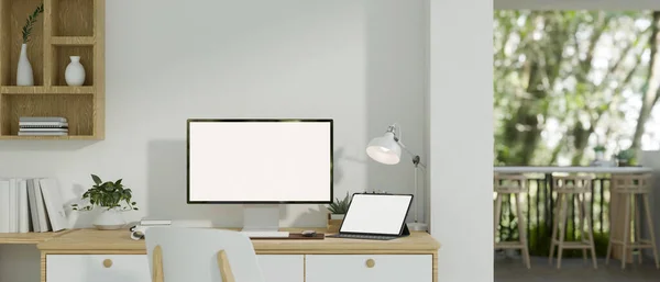 A modern minimalist white home workplace with a computer and a digital tablet white screen mockup on a table against the white wall, a chair, a wall shelf, and decor. 3d render, 3d illustration
