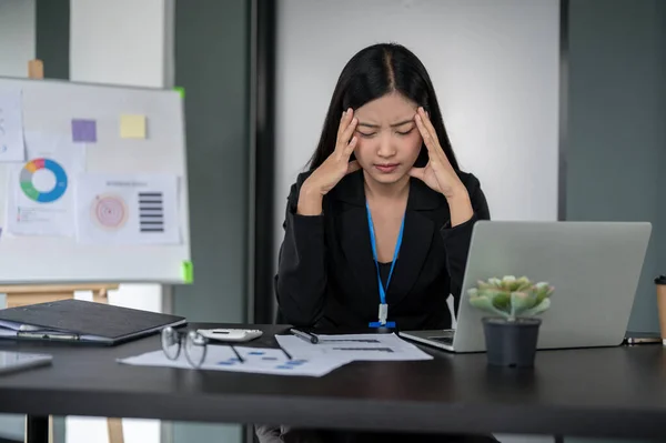 A stressed and confused millennial Asian businesswoman or female financial worker working on her financial project at her desk, thinking pensively about the solution to solve the problems.