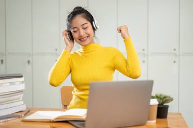 Neşeli ve mutlu bir Asyalı kız üniversite öğrencisi kütüphanede ödev yaparken kablosuz kulaklıklarıyla müzik dinlemekten hoşlanıyor..