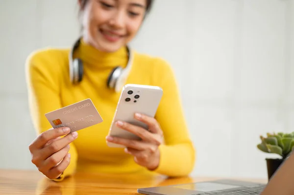 Close-up image of a happy Asian woman holding a credit card and her smartphone, using a mobile banking application to transfer her money or pay bills online. People and financial technology concepts