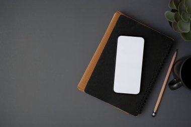 Beyaz ekran akıllı telefon bir kitap, bir kalem, bir kahve kupası, bir saksı bitkisi, ve gri bir arka planda bir kopya alanı. Üst görünüm, düz uzanma