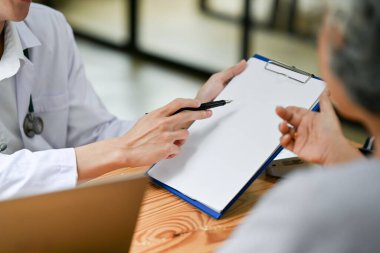 Hastane muayene odasında yaşlı bir bayanla ameliyat sonrası bir tedavi planına danışmanlık yapan profesyonel bir doktorun yakın plan görüntüsü..