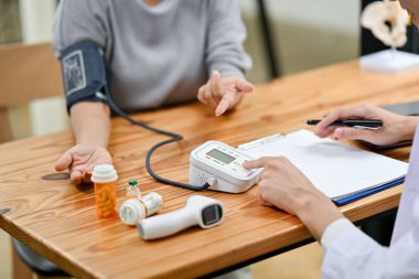 Hastanedeki muayene odasında bir doktorla konuşurken kalp atış hızı ve kan basıncı ölçülen yaşlı bir kadının yakın çekim görüntüsü..