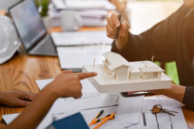 Profesyonel bir Asyalı erkek mimar ofiste bina tasarımlarını tartışırken müşterisine ev modelini gösteriyor. yakın plan resim