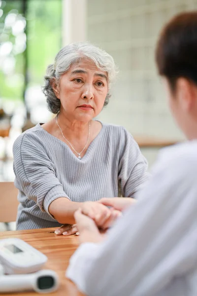 A concerned Asian retired old lady is being diagnosed and checked for pulse on her wrist by a doctor during her medical checkup at a hospital. Health care concept