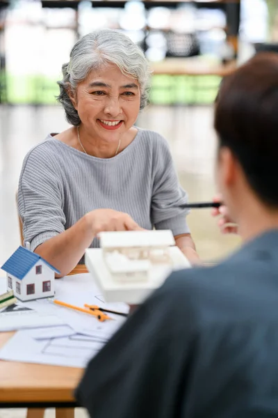 A happy and satisfied Asian retired lady is having a meeting with her architect or interior designer to discuss her house\'s interior design.