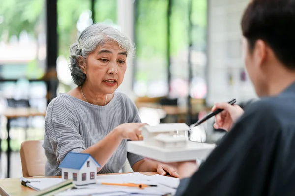 A serious retired Asian lady client is having a serious meeting with her architect or interior designer to complain about her house-building process.