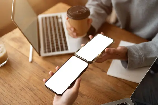 Close-up image of a woman is sharing files or a contact on her smartphone to her friend\'s smartphone while sitting in a coffee shop together. Smartphone white screen mockup. Technology concept