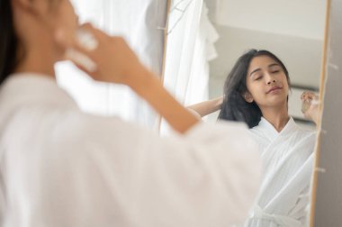 Bornozlu çekici ve güzel bir Asyalı kadın aynanın karşısına parfüm sürüyor, hazırlanıyor. Yaşam tarzı ve güzellik kavramları