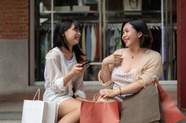 İki çekici ve neşeli Asyalı genç bayan arkadaş şehirdeki alışveriş günlerinde merdivenlerde dinlenirken gülüyor ve sohbet ediyorlar. Yaşam tarzı kavramı