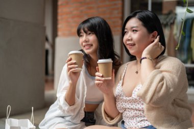 Çekici ve neşeli genç Asyalı iri yarı bir kadın şehirde alışveriş günü boyunca arkadaşıyla merdivenlerde dinlenirken sohbet etmekten ve kahve içmekten zevk alır. Yaşam tarzı kavramı