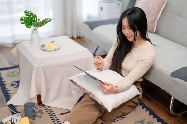 一位漂亮的年轻亚洲女人在客厅里放松的时候用她的数码平板电脑 人与休闲概念 — 图库照片