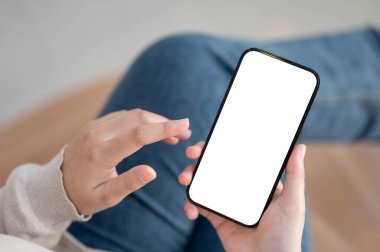 Evin içinde oturan ve akıllı telefonunu mesajları kontrol etmek ya da arkadaşlarıyla sohbet etmek için kullanan bir kadının en iyi görüntüsü. Bir kadının elinde beyaz ekran akıllı telefon modeli var. İnsanlar ve teknoloji kavramları